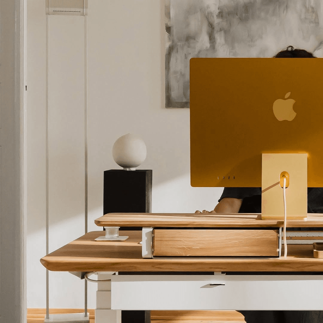 A person working behind a yellow desktop computer at a wooden desk.