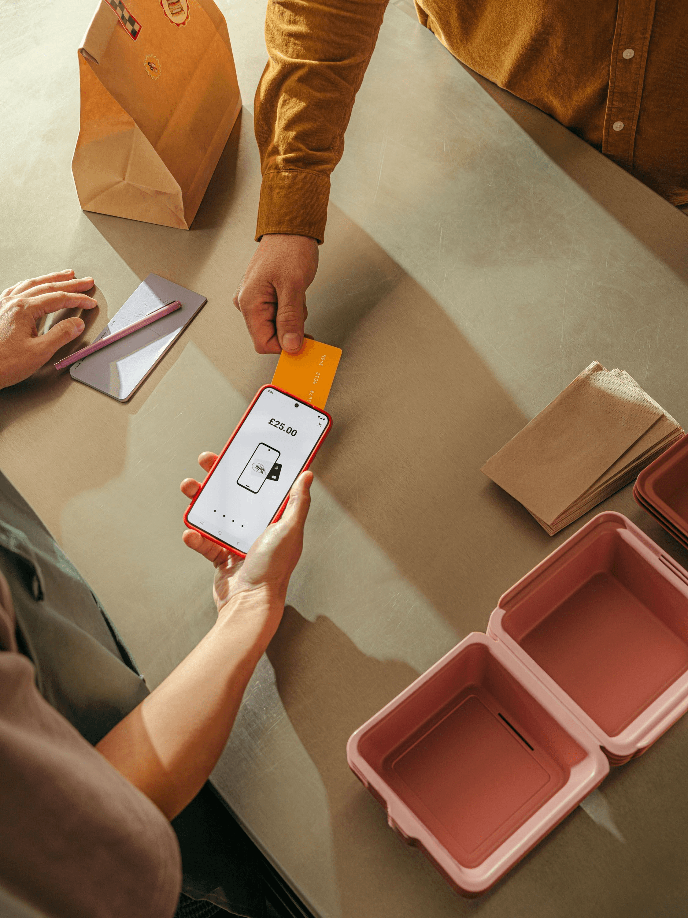 Hands using a phone and payment card at a shop counter.