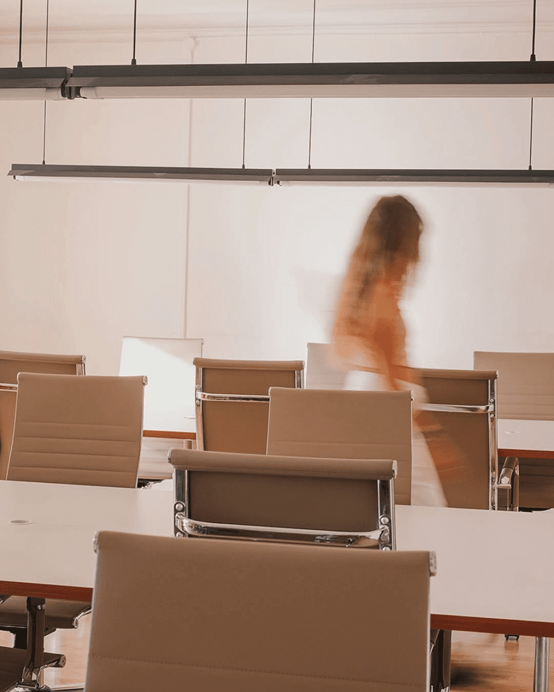 A sunlit workspace with chairs, shared desks, and a person walking through.